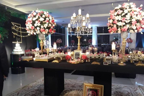 Mesa de doces decorada com flores e candelabros em uma festa no Alpen Festas.