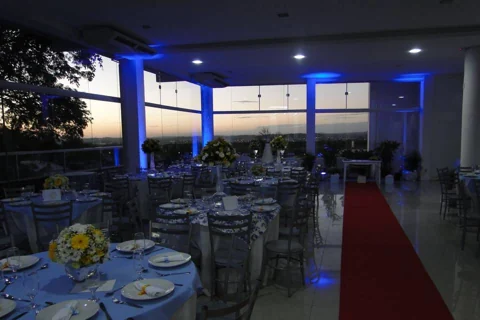 Salão do Alpen Festas com mesas montadas e vista para a cidade ao entardecer.