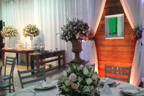 Mesa posta com flores, cadeiras e uma mesa de doces ao fundo no Alpen Festas.